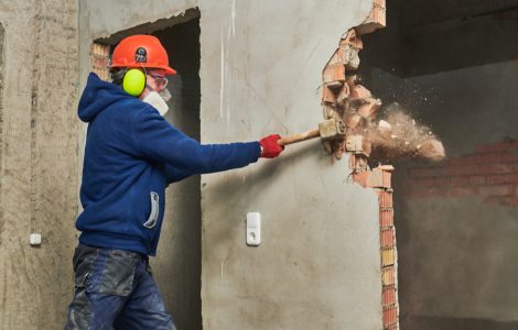 Un ouvrier abat un mur en briques avec son marteau