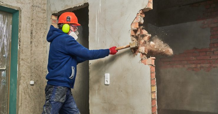 Un ouvrier abat un mur en briques avec son marteau