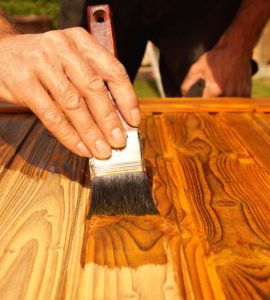 Gros plan sur la main d'un homme appliquant un vernis sur un meuble en bois à l'aide d'un pinceau