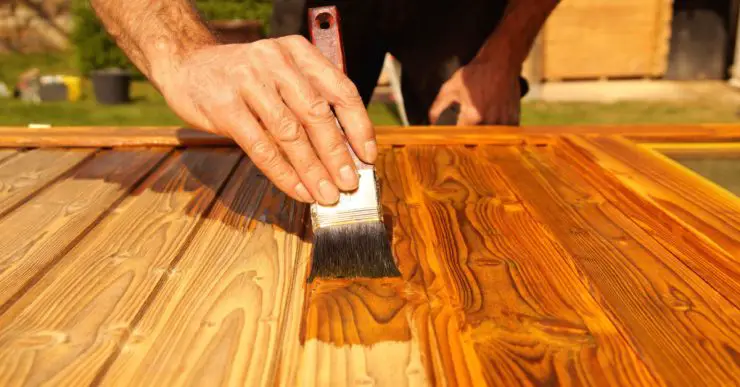 Gros plan sur la main d'un homme appliquant un vernis sur un meuble en bois à l'aide d'un pinceau