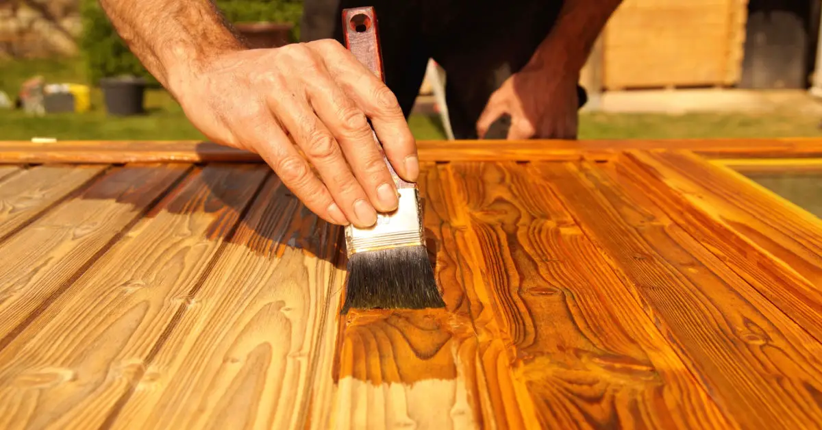 Gros plan sur la main d'un homme appliquant un vernis sur un meuble en bois à l'aide d'un pinceau