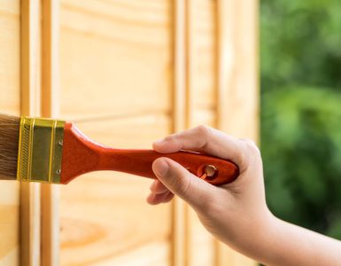 Gros plan sur la main d'une personne peignant la porte en bois à l'aide d'un pinceau