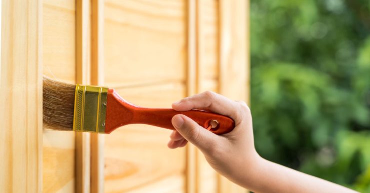Gros plan sur la main d'une personne peignant la porte en bois à l'aide d'un pinceau