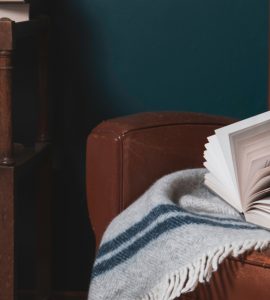 Un livre et une couverture posés sur un vieux fauteuil en cuir marron