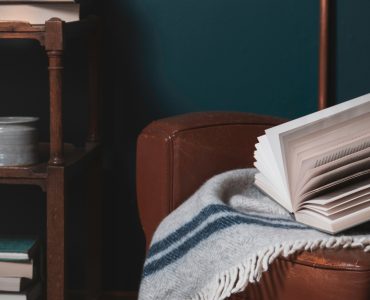 Un livre et une couverture posés sur un vieux fauteuil en cuir marron