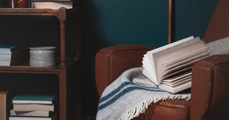 Un livre et une couverture posés sur un vieux fauteuil en cuir marron