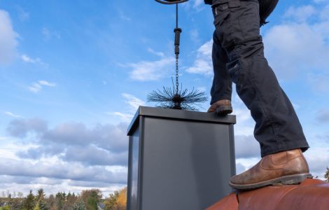 Un homme debout sur le toit nettoie le conduit d'une cheminée à l'aide d'un outil spécial