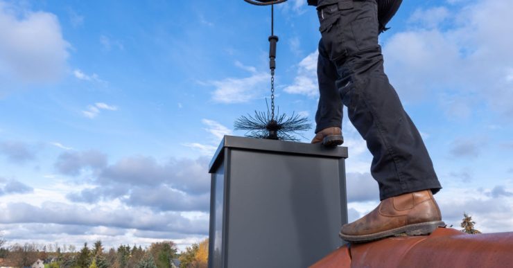 Un homme debout sur le toit nettoie le conduit d'une cheminée à l'aide d'un outil spécial