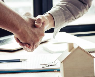 Deux hommes se serrent la main près d'une table avec une maquette de maison dessus