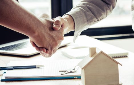 Deux hommes se serrent la main près d'une table avec une maquette de maison dessus