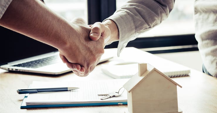 Deux hommes se serrent la main près d'une table avec une maquette de maison dessus