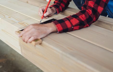 Un homme trace des lignes sur du bois à l'aide d'un crayon et d'une équerre