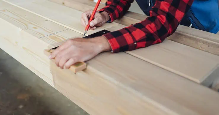 Un homme trace des lignes sur du bois à l'aide d'un crayon et d'une équerre