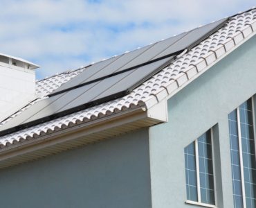 Une maison gris avec des panneaux solaires sur le toit en tuile
