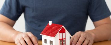 Un homme tenant un dossier sur la table, avec une maquette de maison posée dessus