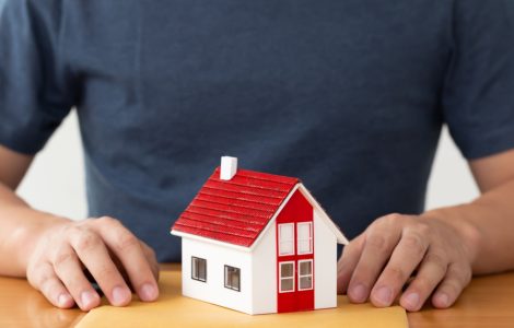 Un homme tenant un dossier sur la table, avec une maquette de maison posée dessus