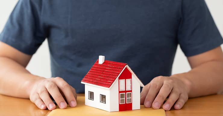 Un homme tenant un dossier sur la table, avec une maquette de maison posée dessus