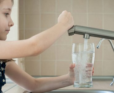 Une petite fille remplit un verre avec de l'eau du robinet