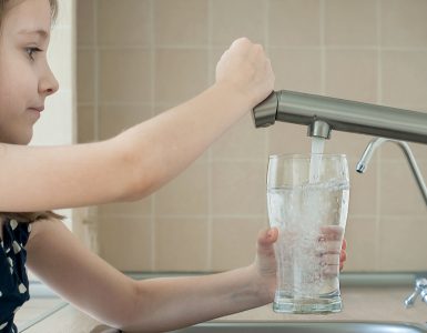 Une petite fille remplit un verre avec de l'eau du robinet