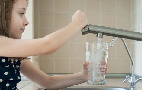 Une petite fille remplit un verre avec de l'eau du robinet
