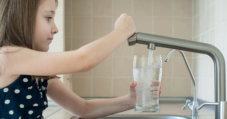 Une petite fille remplit un verre avec de l'eau du robinet