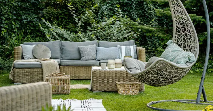 Mobilier en osier avec des coussins gris placés dans le jardin