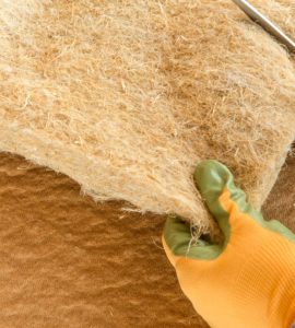 Mains d'un homme en gants jaunes et verts qui découpe un isolant en fibres avec un ciseau