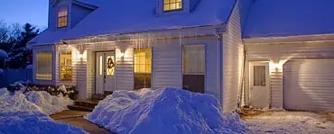 Une maison blanche couverte de neige, avec les lumières allumées