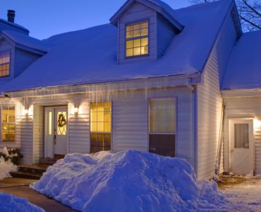 Une maison blanche couverte de neige, avec les lumières allumées