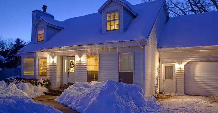 Une maison blanche couverte de neige, avec les lumières allumées