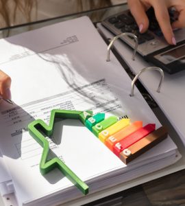 Une femme utilisant une calculatrice, avec une maquette de l’étiquette énergie sur la table