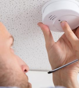 Un homme installe un détecteur de fumée au plafond