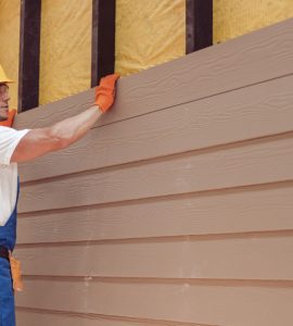 Un homme avec un casque de chantier réalisant le bardage d'une nouvelle maison