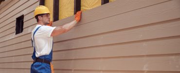 Un homme avec un casque de chantier réalisant le bardage d'une nouvelle maison