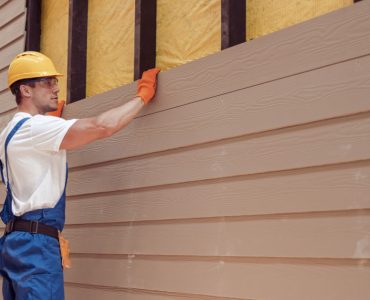 Un homme avec un casque de chantier réalisant le bardage d'une nouvelle maison
