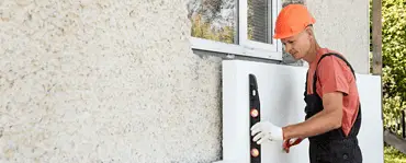 Un homme avec un casque de chantier installe une plaque d'isolation en polystyrène sur la façade