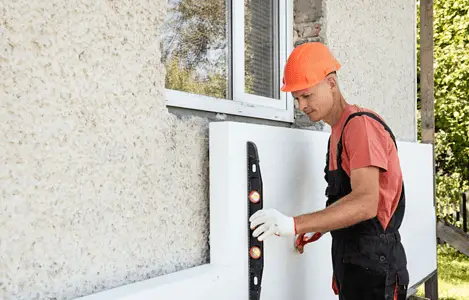 Un homme avec un casque de chantier installe une plaque d'isolation en polystyrène sur la façade