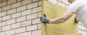 Un homme réalise l'isolation extérieure d'une maison avec des plaques de laine de roche minérale