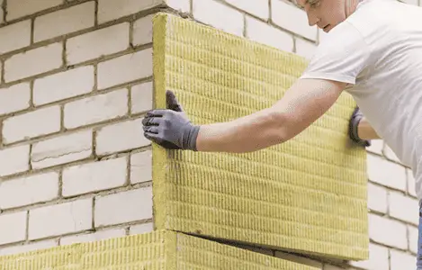 Un homme réalise l'isolation extérieure d'une maison avec des plaques de laine de roche minérale