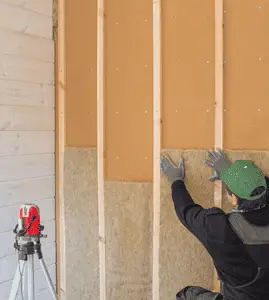 Un homme avec un casque de chantier posant de l'isolant en fibre de bois sur un mur intérieur