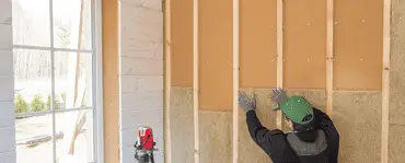 Un homme avec un casque de chantier posant de l'isolant en fibre de bois sur un mur intérieur