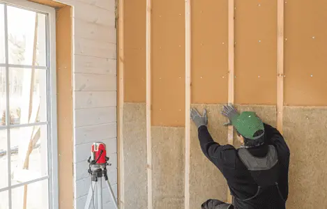 Un homme avec un casque de chantier posant de l'isolant en fibre de bois sur un mur intérieur