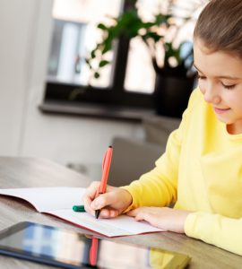 Une petite fille étudie sur la table avec un cahier et une tablette