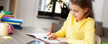 Une petite fille étudie sur la table avec un cahier et une tablette