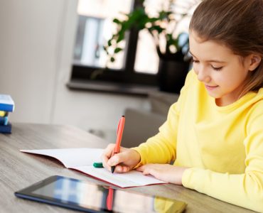 Une petite fille étudie sur la table avec un cahier et une tablette