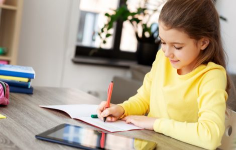 Une petite fille étudie sur la table avec un cahier et une tablette