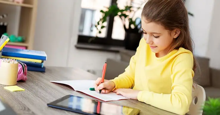 Une petite fille étudie sur la table avec un cahier et une tablette