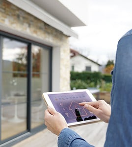 Une femme à l'extérieur d'une maison lance le système domotique sur sa tablette numérique