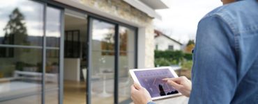 Une femme à l'extérieur d'une maison lance le système domotique sur sa tablette numérique