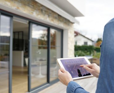 Une femme à l'extérieur d'une maison lance le système domotique sur sa tablette numérique